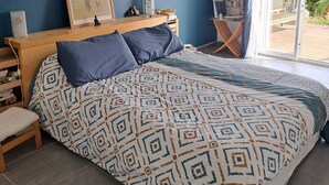 Een slaapkamer met een bed, een bureau, een stoel, een raam met gordijnen en uitzicht op groen.