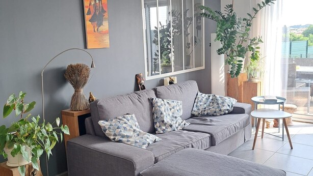 Een moderne woonkamer met een grijze modulaire bank, een groot raam met uitzicht en een decoratief schilderij.