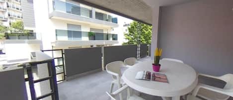A balcony with a round table, chairs, and a potted plant.
