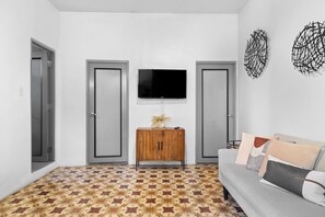 Ein Wohnzimmer mit einem gemusterten Boden, einem grauen Sofa, einer Holzkommode und einem an der Wand befestigten Fernseher.