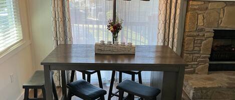 Un coin repas comprenant une table, quatre chaises, un vase avec des fleurs et une cheminée en pierre.