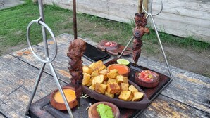 Ein Grillplatz mit Spießen, Kartoffelspalten und Dip-Saucen auf einem Holztisch.
