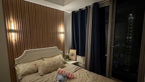 Une chambre à coucher avec un lit, une table de chevet, une fenêtre avec des rideaux et une vue sur un bâtiment à l’extérieur.