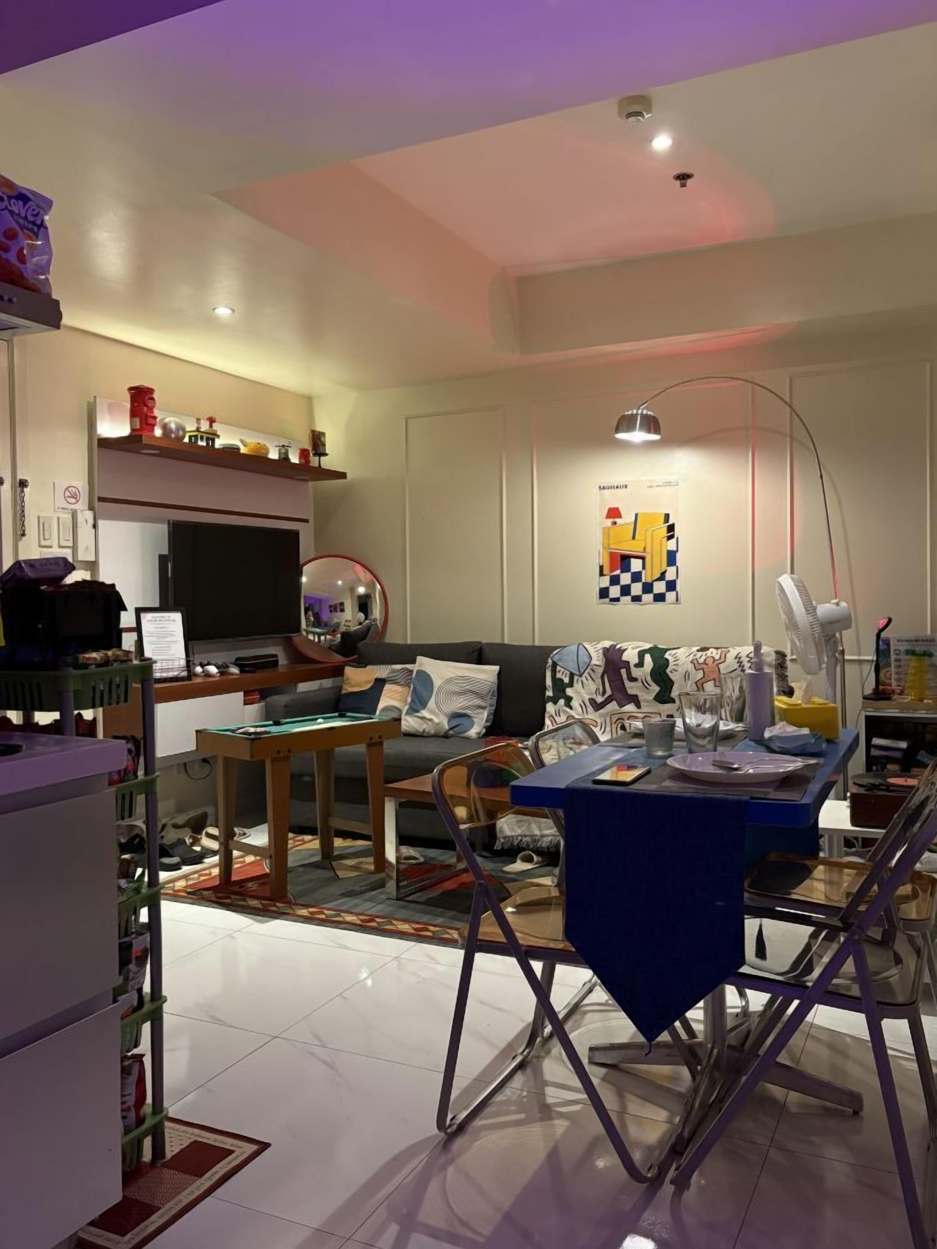 A modern living room with a sofa, a dining table, and a kitchen area with a microwave and a kettle.