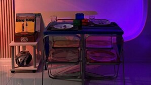 Une pièce avec une table mise pour deux, une affiche accrochée au mur et un haut-parleur posé sur une étagère.