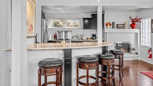 A modern kitchen with a central island, bar stools, a fireplace, and a stone wall. - Kings Beach Cabin w/ Panoramic Lakeview & Forest (Kings Beach)