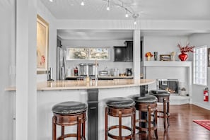 A modern kitchen with a central island, bar stools, a fireplace, and a stone wall. - Kings Beach Cabin w/ Panoramic Lakeview & Forest (Kings Beach)