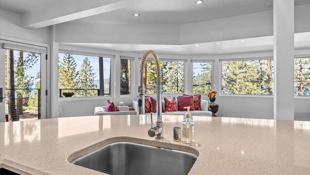 A modern kitchen with a large island, stainless steel sink, and a view of trees through large windows. - Kings Beach Cabin w/ Panoramic Lakeview & Forest (Kings Beach)