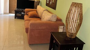 A living room with a sofa, a television, a bamboo lamp, and a painting on the wall.