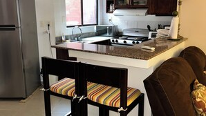A kitchen with a refrigerator, stove, and microwave. There are two chairs with striped cushions.