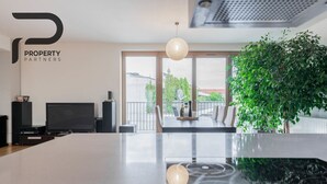 Una cocina moderna con una isla grande, un comedor con sillas, un televisor y un amplio ventanal con vistas a la ciudad.