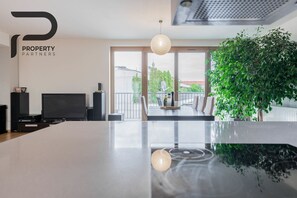 A modern kitchen with a large island, a dining area with chairs, a television, and a large window with a view of the city. - Angel Plaza Kraków Apartment 140m2 / 5 minutes from the main square (Kraków)