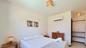 A hotel room with a bed, bedside lamp, air conditioning unit, wooden cabinet, and a towel on the bed. - Beach-home Pontal de Maceio (Fortim)