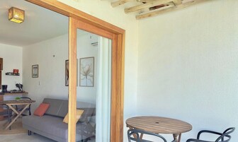 Um quarto com porta de madeira, uma mesa redonda de madeira, um sofá cinzento e uma pequena mesa redonda com uma planta.