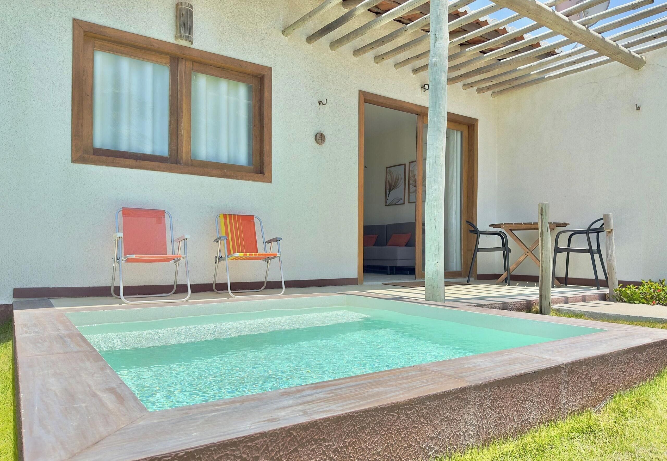 A swimming pool with two chairs, a table, and a covered patio area.