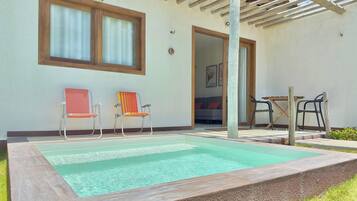 A swimming pool with two chairs, a table, and a covered patio area.