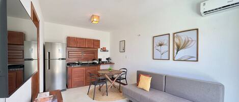 Un espacio habitable compacto con kitchenette, un sofá gris, una mesa de comedor con sillas y un televisor de pantalla plana.