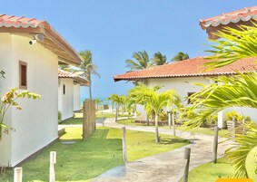 Um resort com vários edifícios, céu claro e um caminho ladeado por palmeiras.