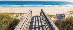 Une promenade en bois mène à une plage où un panneau d’avertissement rappelle de ne pas marcher sur les dunes.