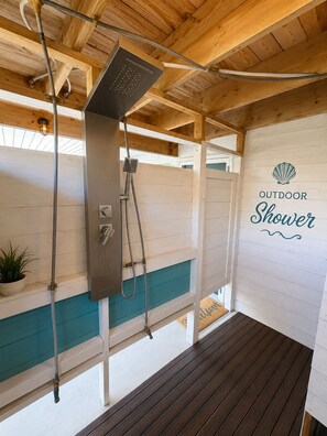 An outdoor shower area with a wooden ceiling and walls, a metal showerhead, and a sign that reads 'OUTDOOR Shower'.