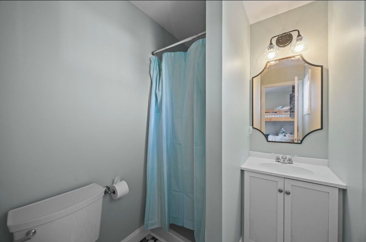 A bathroom with a toilet, a shower curtain, and a vanity with a mirror.