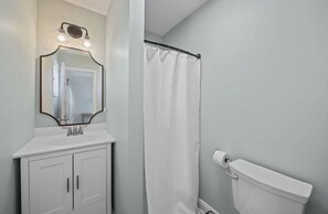 A bathroom with a white sink, a mirror with lights, a shower curtain, and a toilet.