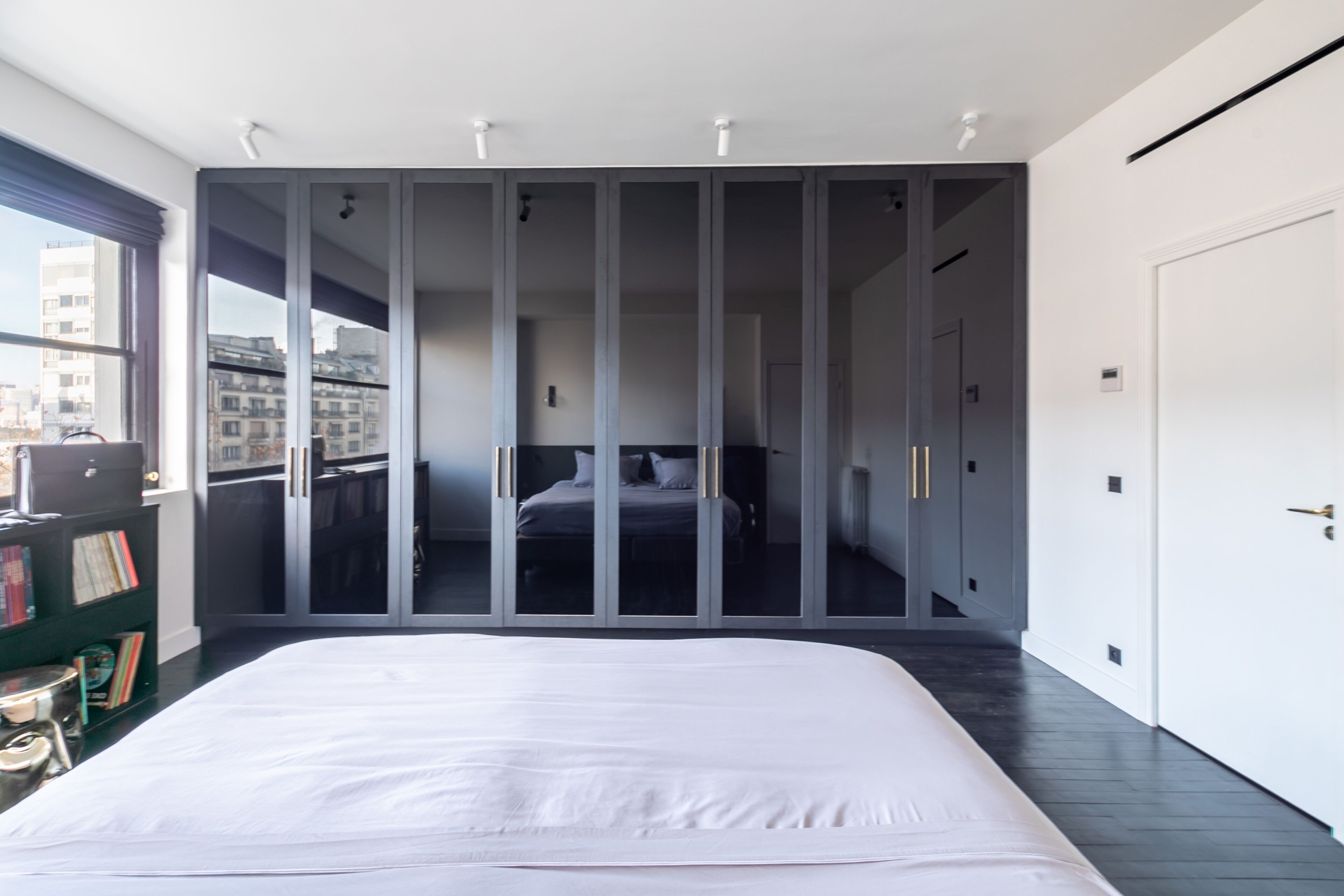 Une chambre à coucher moderne, dotée d’un grand lit, d’une armoire et offrant une vue sur la ville grâce à une porte vitrée.