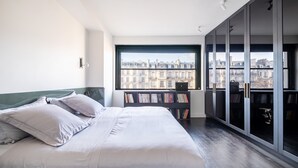 A bedroom with a bed, a bookshelf, and a view of buildings through a large window. - Victor Hugo Design - One Bedroom Apartment, Sleeps 2 (Paris)