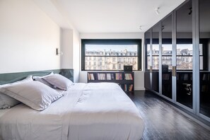 A bedroom with a bed, a bookshelf, and a view of buildings through a large window. - Victor Hugo Design - One Bedroom Apartment, Sleeps 2 (Paris)