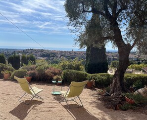 A patio with two chairs and a table, surrounded by potted plants and a large tree. - La Bastide Matisse – Piscine et vue panoramique (Vence)