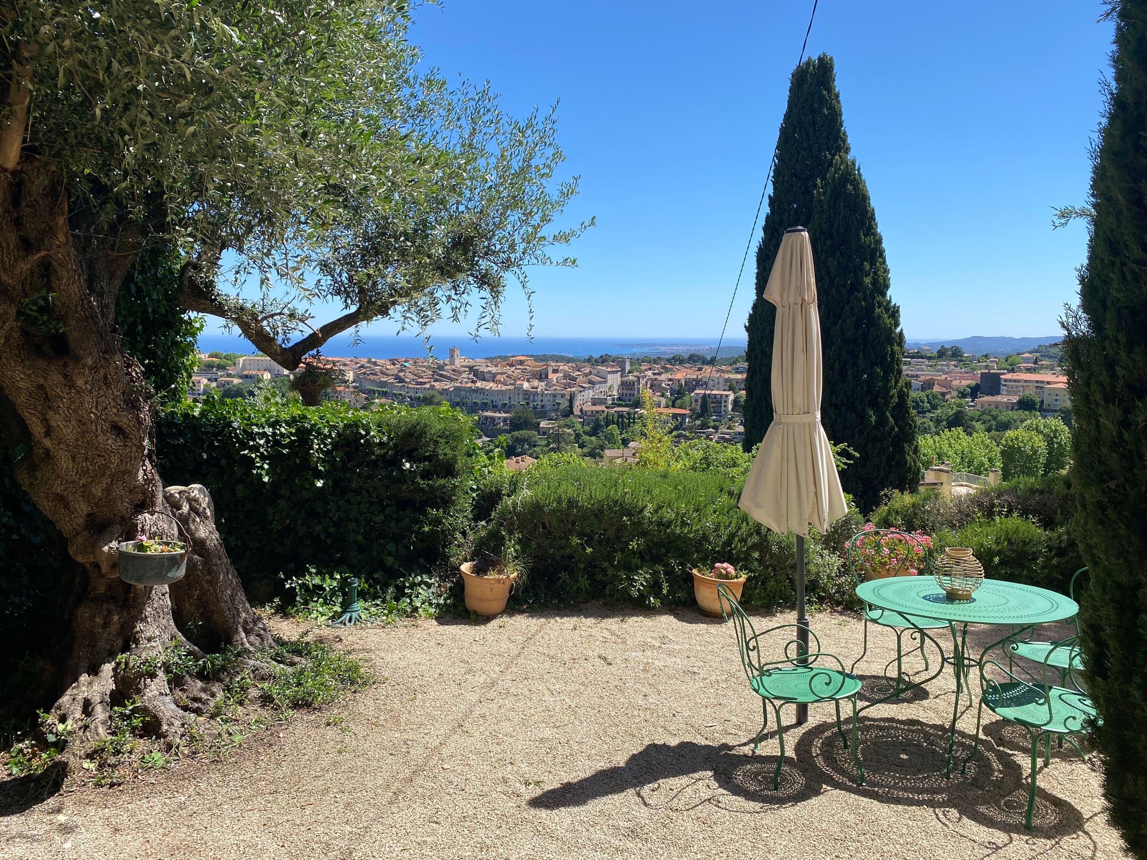 Une terrasse avec une table et des chaises, un parasol suspendu, et une vue sur la ville et la mer.