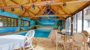 Un espacio al aire libre techado con piscina, mobiliario de madera y un mural con motivo de una playa.