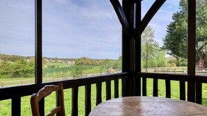 Una silla y una mesa de madera en un balcón con vistas a un paisaje verde y edificios al fondo.