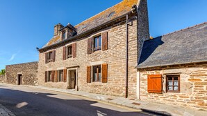 A stone building with a paved street, a clear sky, and a visible door. - La Maison des Seigneurs les pieds dans l'eau (Le Conquet)