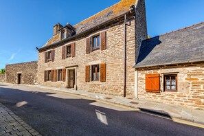 A stone building with a paved street, a clear sky, and a visible door. - La Maison des Seigneurs les pieds dans l'eau (Le Conquet)