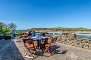 An outdoor patio with a table set for dining, overlooking a coastal area with a stone wall and a view of the sea. - La Maison des Seigneurs les pieds dans l'eau (Le Conquet)