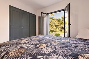 Ein Schlafzimmer mit Bett, einer Tür und Blick auf Palmen.