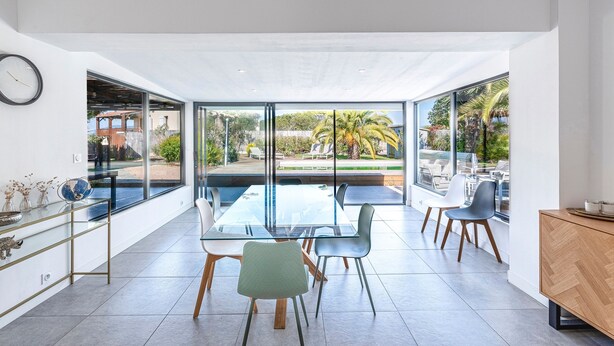 Un espace repas moderne avec une table en verre, des chaises et une vue sur l’extérieur.