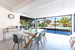 Ein moderner Essbereich mit Glastisch, Stühlen, einer Uhr und Blick auf Pool und Garten.