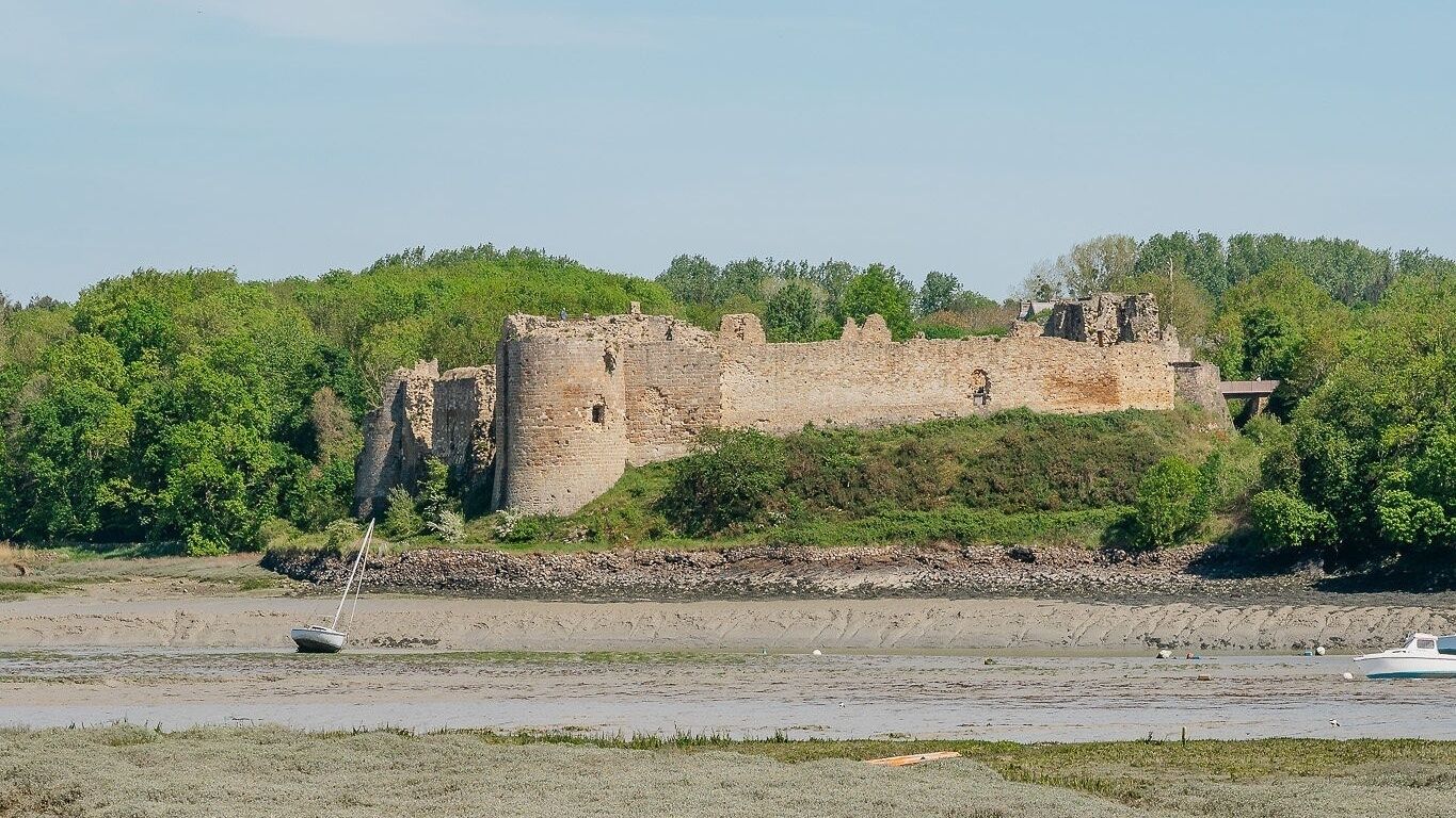 Un castello storico in pietra circondato da vegetazione, situato vicino a un corso d'acqua.