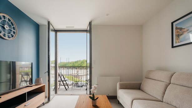 Un salon moderne avec un téléviseur, un canapé, une table basse et une vue sur un espace extérieur, accessible par une porte vitrée.