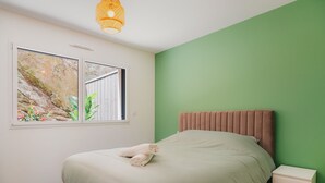 Una camera da letto con un letto, un comodino, una finestra vista verde e un lampadario.