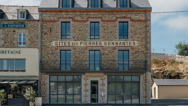 Un edificio con facciata in pietra, diverse finestre e un cartello con su scritto 'GITES DES PIERRES SCONNANTES'.