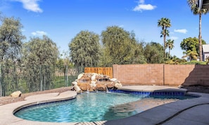 A swimming pool with a waterfall feature, surrounded by a brick wall and a wooden fence. - Spacious 5-bedroom house with AC in beautiful Gilbert with Golf Course View (Gilbert)