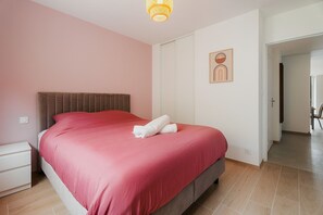 A bedroom with a bed, a nightstand, a wall art piece, and a door leading to another room. - Gites Les Ebihens - Pointe de l'Isle (Saint-Cast-le-Guildo)