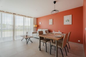 A modern living room with a dining area, large windows, and a view of the outdoors. - Gites Les Ebihens - L'Arguenon (Saint-Cast-le-Guildo)
