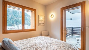 A bedroom with a large bed, a chair, a window with a view of a snowy landscape, and a door leading to an outdoor area. - Cosy Angelus, 4-person apartment 5 minutes from the slopes, mountain view terrace, parking. (Saint-Jean-de-Sixt)