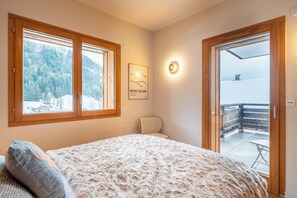 Ein Schlafzimmer mit einem großen Bett, einem Sessel, einem Fenster mit Blick auf eine verschneite Landschaft und einer Tür zu einem Außenbereich.