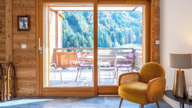 A wooden interior with a sliding glass door leading to an outdoor patio with chairs and a table. - Cosy Angelus, 4-person apartment 5 minutes from the slopes, mountain view terrace, parking. (Saint-Jean-de-Sixt)