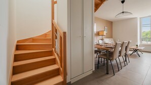 A staircase leading to a dining area with a table set for four, a chair, and a small table with a plant. - Gites Les Ebihens - Pierres Sonnantes (Saint-Cast-le-Guildo)
